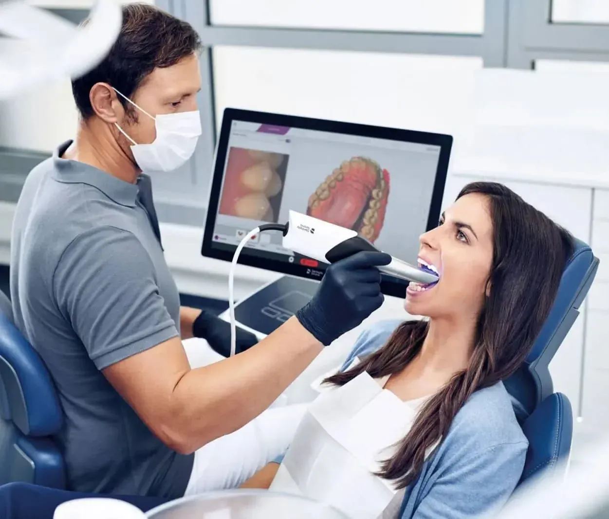 Dentist scanning a patient's teeth with an intraoral scanner while a 3D model displays on a monitor